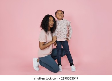 Indoor studio shot of pleasant young African woman mother and her cute adorable little daughter, wearing bright trendy casual clothes, posing together on pink background. - Shutterstock ID 2190363049