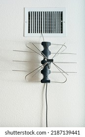 Indoor TV Antenna Hanging By Wire Coat Hanger From Heating Duct On White Textured Wall.