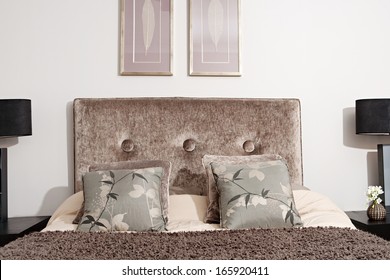 Indoors Designer Decoration View Of A Velvet Bed Head In An Elegant Hotel Bedroom With Lamps And Side Tables, Cushions And Pillows. Home Interior With No People.