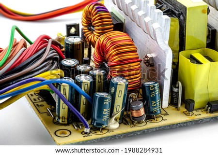 Induction coil, toroidal coil on a ring with visible copper helix and capacitors, mounted on a printed circuit board in a computer power supply.