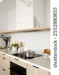 Induction stove in kitchen. Cooking food at home concepts. Stainless steel pot on glass ceramic stovetop. Modern interior with wood cabinets and a marble countertop, vertical shot