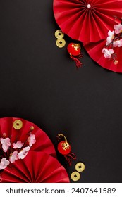 Indulging in the exuberance of the Chinese New Year festival. Top view vertical photo of folding fans, sakura, traditional coins, lanterns on black background with promo spot