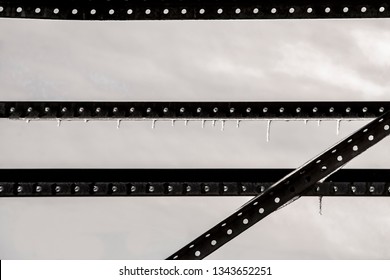 Industrial almost abstract low saturation background of stark metal strips with holes against grey sky with icicles hanging