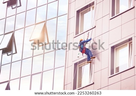 Industrial alpinism. A window cleaner works on the facade of a high-rise office building. Reflection of the sun's rays in the glass. Sunny summer day.