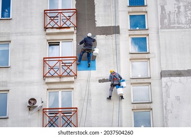  Industrial alpinist at height on rope, plastering wall with trowel. Industrial climber repairing house facade. Rope access job, construction workers repair and restore facade of high building.