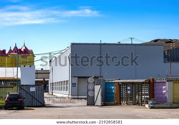 Industrial area. Barrier gate at entrance to\
industrial area. Factory or factory checkpoint. Industrial area in\
summer weather. Hangar with gate. Two-story warehouse building\
behind barrier gate