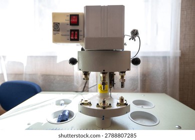 An industrial automatic button and rivet setting machine with red rocker switches on the electrical control panel is positioned on a worktable surface inside a manufacturing textile workshop