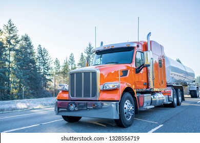 Industrial Big Rig Low Cab Bonnet Orange Classic Popular American Semi Truck Transporting Commercial Liquid Cargo And Fuel In Tank Semi Trailer Moving On The Winter Frosty Road With Frost Trees