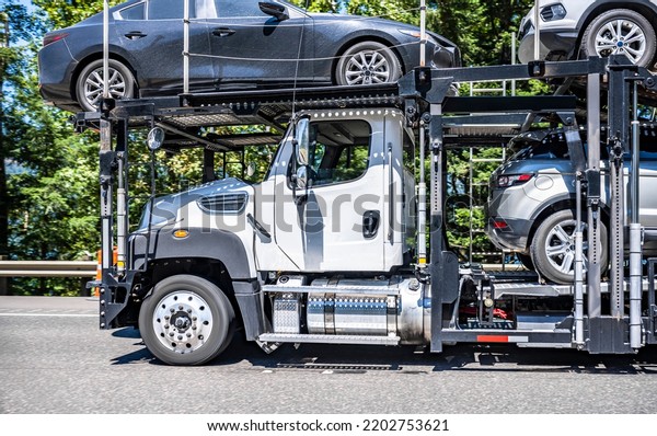 Industrial big rig white day cab car hauler semi\
truck tractor transporting cars on the hydraulic two level semi\
trailer driving on the one way highway road in green Columbia Gorge\
Recreation area