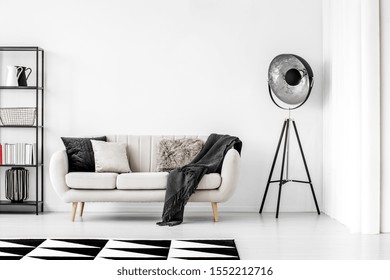 Industrial Black Lamp Next To Beige Couch With Blanket And Pillows, Copy Space On Empty White Wall