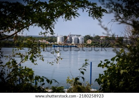 Industrial buildings and storage containers of the port of Giurgiu in Romania seen between branches of a trees on the other side of Danube river in the city of Ruse, Bulgaria