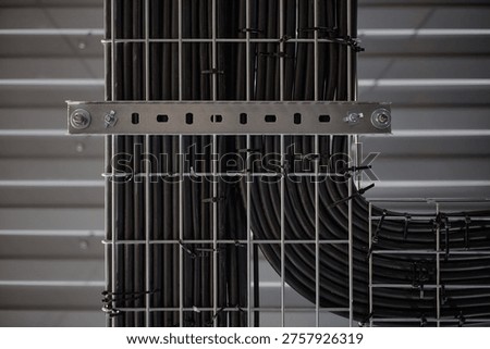 Industrial cable tray system supporting organized black electrical cables running vertically and horizontally along metal grid structure in modern facility interior