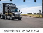 Industrial carrier black big rig semi truck tractor with extended cab for truck driver rest transporting cargo in dry van semi trailer running on the crossroad intersection with traffic light