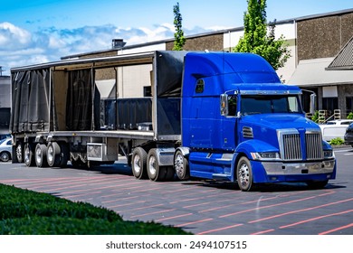 Industrial carrier blue big rig semi truck with extended cab for truck driver rest unloading delivered cargo from open Conestoga curtain-side semi trailer standing on industrial warehouse parking lot - Powered by Shutterstock