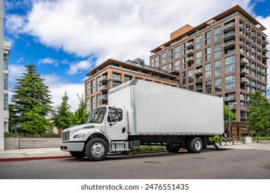 Industrial carrier middle duty day cab rig semi truck with box trailer for local freights standing with open back door on the urban city street making delivery to customer in multilevel apartment