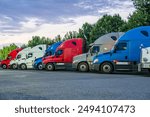 Industrial carriers big rig semi trucks with semi trailers standing for rest in row on the truck stop parking lot with turned on lights at twilight time to be ready to continue the route by morning