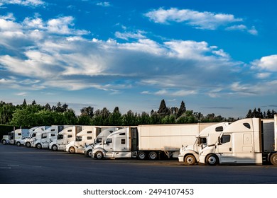 Industrial carriers big rig semi trucks with semi trailers standing for rest in row on the truck stop parking lot with turned of engines at day time to be ready to continue the route after the rest