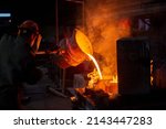 Industrial chill casting. Two workers filling out mold with molten metal in factory.