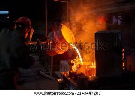 Industrial chill casting. Two workers filling out mold with molten metal in factory.
