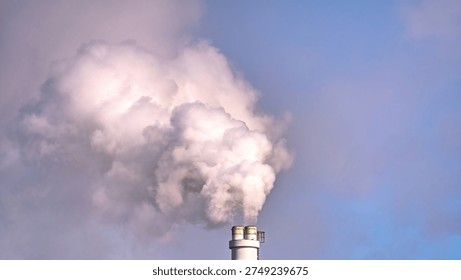Industrial chimney stack emitting thick white smoke against a blue sky. Concept of air pollution, CO2 emissions, climate change and environmental impact from power plant or factory