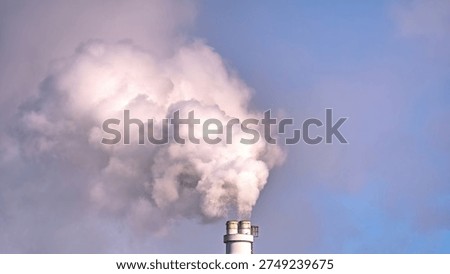 Industrial chimney stack emitting thick white smoke against a blue sky. Concept of air pollution, CO2 emissions, climate change and environmental impact from power plant or factory