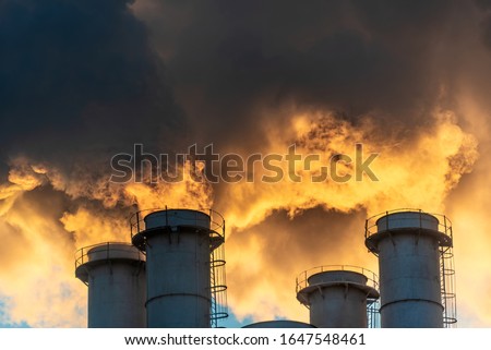 Industrial chimneys spewing smoke and soot in the blue sky polluting the air and causing global warming and climate change with greenhouse gasses and CO2 emissions