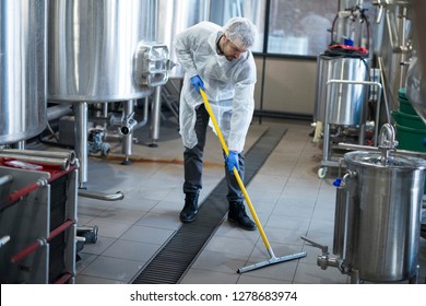 Industrial cleaning service. Professional cleaner wearing protection uniform cleaning floor of production plant.