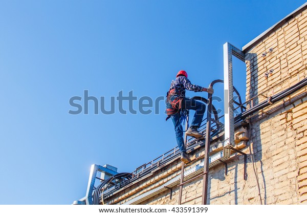 Industrial climber climbs up the stairs to the roof.\
worker in harnesses for working at heights climbs onto the roof.\
copy space for your\
text