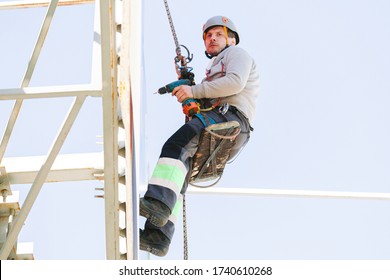 Industrial Climber In Helmet And Overall Working On Height. Risky Job. Professional Worker