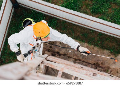 Industrial climber in helmet and white uniform spraying anti-rust liquid on metal construction. Professional worker doing his risky job on height. Top view