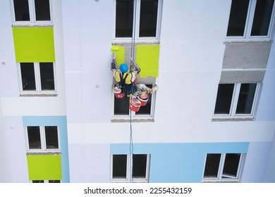 An industrial climber paints the facade of a multi-story building with colorful facade paints. Drone photography. - Shutterstock ID 2255432159