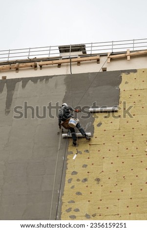 Industrial climber performs work on the insulation of the facade of a residential building.