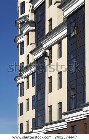 Industrial climber in protection outfit cleaning window glass on the beige vertical wall