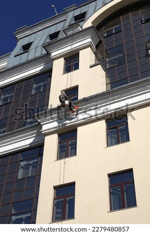Industrial climber in protection outfit on the beige wall cleaning window glass