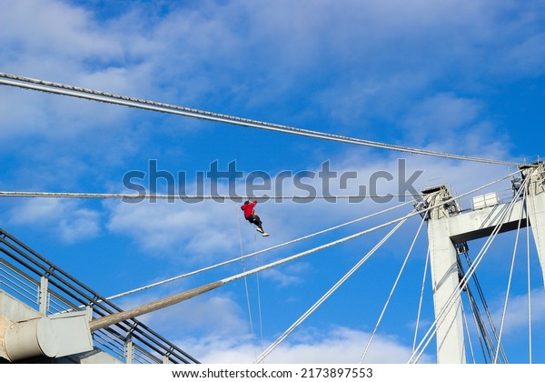 Industrial climber working at height on a\
suspension bridge against blue sky\
background