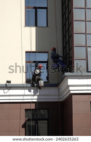 Industrial climbers in protection outfit cleaning window glass on the beige vertical wall closeup