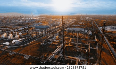Industrial complex with pipes and structures under a setting sun. Workers manage operations at an industrial site during the evening. The sun sets over the landscape.