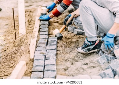 Industrial construction worker paving road with granite cobblestone using sand and rubber hammer