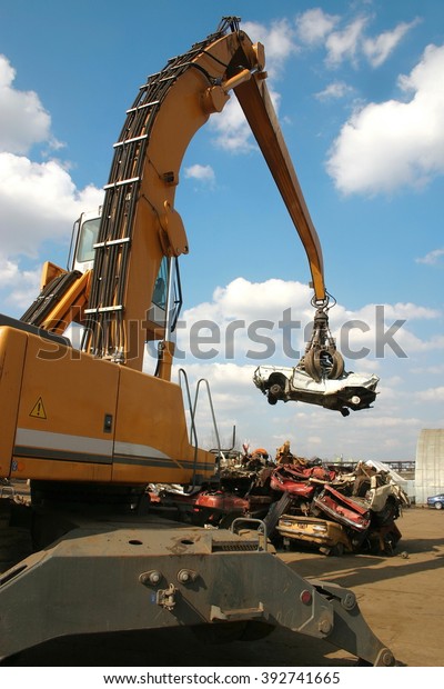Industrial crane claw grabbing old car for\
recycling metal