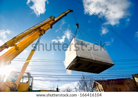 Industrial Crane operating and lifting an electric generator against sunlight and blue sky