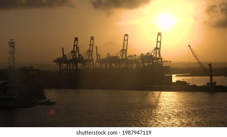 Industrial Cranes In Waterfront Cargo Port. Sunset And Cargo Cranes In The Seaport.