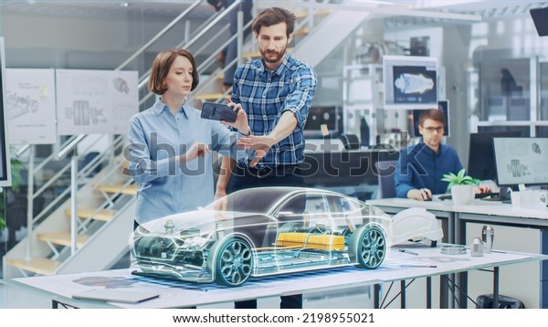 Industrial\
Design: Automotive Engineer and Designer Working on 3D Electric Car\
Design, Using Smartphone with Augmented Reality. Graphical Engine,\
Battery, Chassis, Body Collect into\
Vehicle