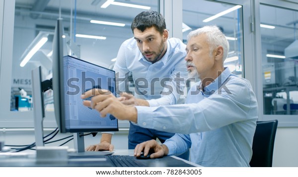 Industrial Designer Has Conversation
with Senior Engineer While Working in CAD Program, Designing New
Component. He Works on Personal Computer with Two
Monitors.