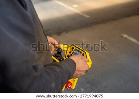 Industrial employee using a wireless remote controller to operate heavy overhead crane equipment inside a manufacturing warehouse.