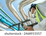 Industrial engineer adjusting pipeline valve with radio communication on construction site. Engineer on urban construction site using radio to coordinate with team on a sunny industrial rooftop.