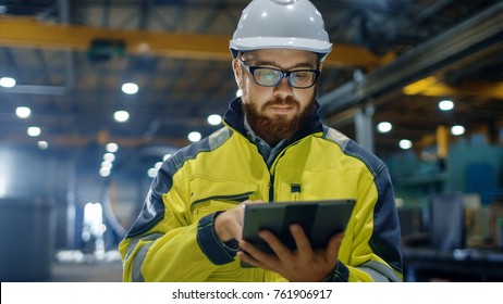 Industrial Engineer In Hard Hat Wearing Safety Jacket Uses Touchscreen Tablet Computer. He Works At The Heavy Industry Manufacturing Factory.