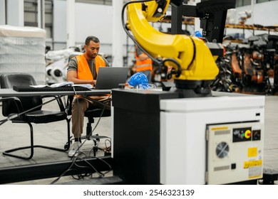 Industrial engineer programming a robotic arm using a laptop, working on automation processes in a modern factory setting, improving efficiency and productivity - Powered by Shutterstock