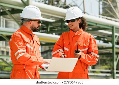 Industrial engineer team checking refinery workflow with laptop and radio communication near pipeline system, discussing safety compliance and operational monitoring inside petrochemical facility