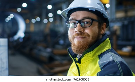 Industrial Engineer Wearing Hard Hat,  Safety Jacket and Glasses Smiles on Camera. He Works in Big Heavy Industry Factory.
