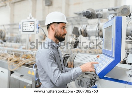 Industrial engineer wearing hardhat operating machinery in modern manufacturing plant, showcasing expertise in production process